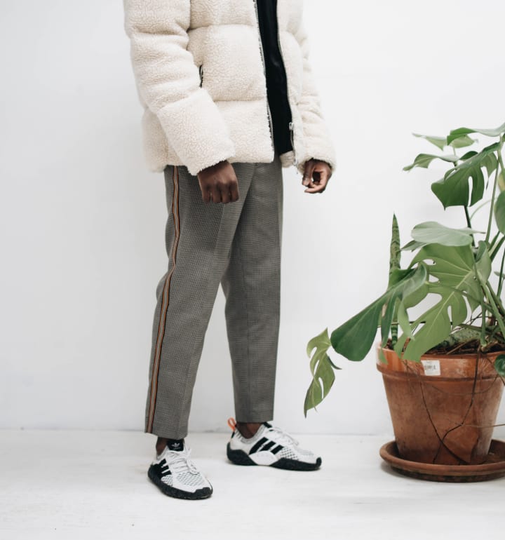 Ung man med en vit dunjacka och gr&aring;a byxor modellerar i en butik.